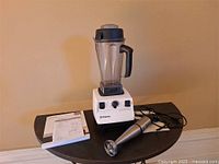 Vitamix blender with jar, immersion blender and manual on table