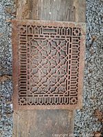 Overall view of rectangular cast iron grate on wooden plank showing full ornate pattern