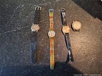 Group shot of four wristwatches on dark surface