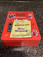 Closed red metal locker tin showing title of all three films