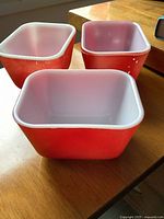 Three red Pyrex refrigerator dishes on wooden surface
