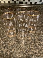 Five clear highball glasses with frosted diamond pattern and gold rims on countertop