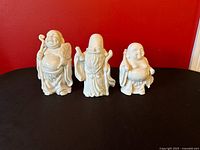 Front view of three ivory glazed ceramic Buddha figures against red backdrop