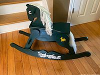 Left side view of dark green wooden rocking horse showing yarn mane, painted bird and floral accents