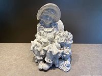 Front view of white plaster statue depicting seated girl holding roses