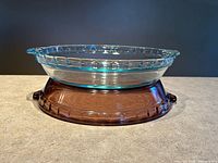 Blue-tinted pie dish resting upside on purple smoked glass dish, side view showing color and scalloped rim