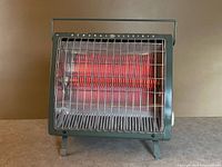 Front view of heater powered on showing red heating elements, grill, feet, handle