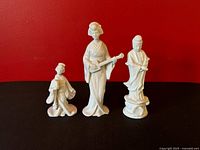 Group shot of all three white porcelain figurines against red background