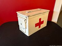 Front angled view showing white metal box, red cross decal, latch and handle
