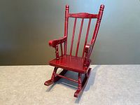 Front view showing red wooden miniature rocking chair with spindles, slatted back, and rocker feet