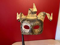 Front view of jester mask showing sheet-music points, bells, metallic detailing