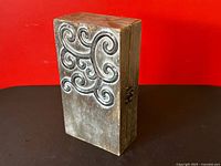 Front view of closed wooden box showing full embossed metal scroll lid and clasp