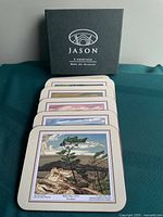 Six coasters with artwork lined in front of Jason box