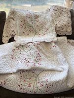 Quilt and pillow shams draped over sofa showing cherry blossom design and scalloped edges