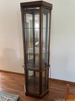 Full view of tall corner curio cabinet with glass door and shelves