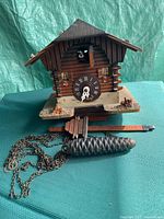 Front view of wood chalet cuckoo clock with dial, chains, pine-cone weight, pendulum