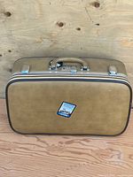 Front view of tan hard-shell suitcase showing travel sticker and overall condition