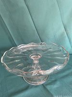 Top view of clear glass pedestal cake stand showing scalloped rim and swirl pattern