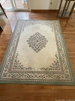 Full view of ivory rug with sage border and floral medallion