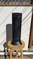 Front view of black Honeywell ceramic tower heater on stool