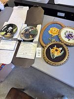 Overall lot view showing both plates with certificates and three framed needlepoints