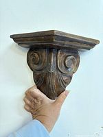 Front view of one carved wooden wall shelf held by hand for scale