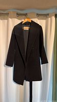 Full front view of black wool coat on hanger