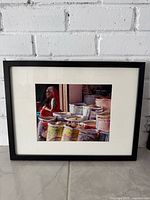 Framed photograph of market vendor with spice sacks, black frame, white mat