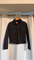 Front view of black denim sherpa-lined trucker jacket on hanger