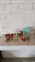 Group shot of approx. 12 perfume/cologne bottles on white brick hearth