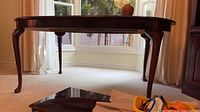 Side view showing dark wood dining table, curved legs, no leaves inserted