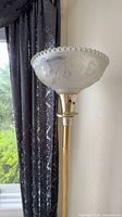 Top portion of gold-tone lamp showing frosted embossed glass shade and upper column