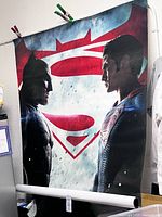 Full view of rolled poster showing Batman and Superman imagery