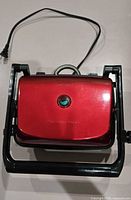 Top view of red Hamilton Beach sandwich maker in black floating frame, power cord visible