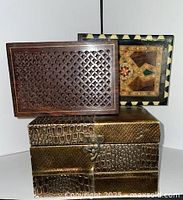 Group shot showing three decorative boxes stacked: carved lattice wood, inlaid marquetry wood, gold faux reptile