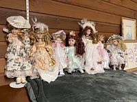 Seven porcelain dolls lined on shelf against wood wall
