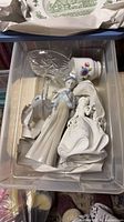 Plastic bin showing standing and seated porcelain figurines, Royal Albert teacup, crystal goblet