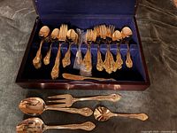 Open case displaying gold-plated flatware pieces and serving utensils