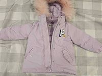Full view of lilac winter jacket showing front, pockets, hood, faux fur trim, and bear patch