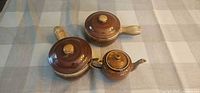 Top view of two lidded soup crocks and mini teapot showing brown drip glaze and beige rims
