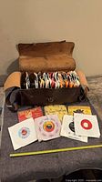 Open leather case filled with 45 rpm records, some records and sleeves displayed in front with measuring tape for scale