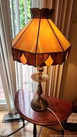 Full view of lamp on table, shade illuminated, shows brass base and power cord