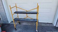 Overall view of yellow two-step scaffold showing platforms and caster wheels