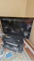 Front view of Sony Bravia TV on black stand with VHS/DVD combo and remotes visible
