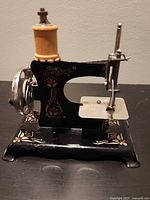 Left front view of miniature sewing machine showing floral decals and wooden spool pin