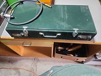 Closed green Coleman stove with handle and regulator hose on top