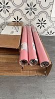 Three sealed pink gift wrap rolls alongside boxes containing additional rolls