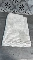 Folded white textured bath rug with Casaluna tag visible