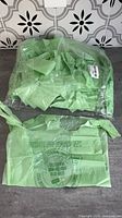 Two sealed bundles of folded green compostable bags in clear packaging