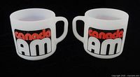Front view of two Canada AM milk glass mugs displaying logo